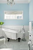 Free-standing bathtub in bright bathroom with pale blue walls and marble tiles