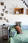 Bed, metal shelving, old wine crates used as shelving modules and name made of decorative letters in teenager's bedroom