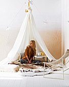 Woman is sitting under the hanging tent with furs and coffee table