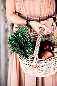 Frau im nostalgischen Kleid trägt Korb mit Rosmarinzweigen und Ernte