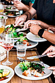 Gedeckter Tisch mit sommerlichen Salaten und Fleich, Hände beim Essen