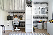 Loft bed above desk in child's bedroom with black-and-white wall; boy seated at desk
