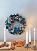 Candles in front of a wreath made from painted pine cones