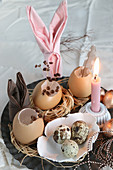 Easter arrangement of small straw nests, Easter bunnies made from folded napkins, quail eggs in ceramic dish and lit candle
