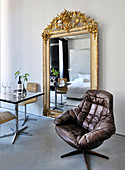 Bistro table and chairs next to large mirror with ornate gilt frame an leather swivel armchair