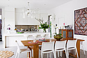 White fitted kitchen with island and wooden dining table with white chairs