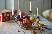 Apples in wire basket with four lit white candles on rim
