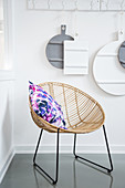 Colourful cushion on rattan easy chair below chopping boards hung from row of hooks