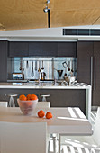 Oranges on white dining table in front of charcoal fitted kitchen with island counter