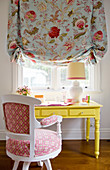 Yellow desk below window with floral Roman blind