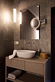Washstand with countertop sink below mirror with infrared heating in bathroom with dark tiles