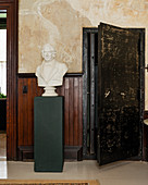 Plaster bust on green plinth in room with wooden wall panelling and large walk-in safe