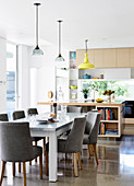 Essbereich mit grauen Polsterstühlen in heller, offener Küche mit Theke und poliertem Betonboden