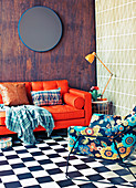 Red leather couch with pillows and plaid, side table and chair with floral cover on checkered pattern floor