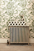 Ornament on top of old radiator against green-patterned wallpaper