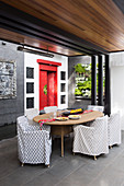 Überdachte Terrasse mit Rattantisch, Hussenstühlen, vertikaler Bepflanung und roter, chinesischer Tür