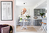 Blick in offene Küche mit hellgrauen Schränken, rundem Esstisch und Designerstühlen, im Vordergrund antiker Sessel und New-York-Poster