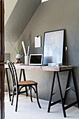 Desk made from trestles against grey wall below sloping ceiling