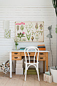 Wooden desk and chair, botanical poster and lamp on white-painted wooden wall