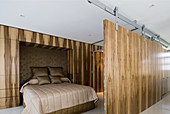 Elegant double bed in sleeping area screened by sliding wooden elements