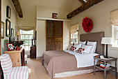 Cushions on double bed with headboard in bedroom with seagrass matting and red Juju hat on wall