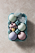 Mit Naturfarben gefärbte Eier, bunte Schokoladeneier und Feder in blauem Eierkarton