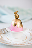 Bunny on top of pink Easter egg with gold leaf