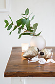 Christmas decorations, leafy branches in spherical vase and tealight on wooden table