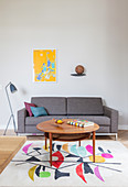 Round table on brightly patterned rug in front of grey sofa