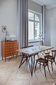 Dining table with wooden top and chairs in front of chest of drawers in period apartment