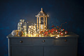 Lantern, glass jars, branch of berries and fairy lights on top of chest of drawers