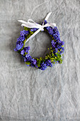 Small wreath of grape hyacinth flowers with white ribbon on grey surface