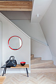 Bag and bowl on bench below round mirror in stairwell