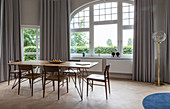 Dining table with wooden top and chairs in front of arched window in period apartment