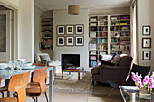Interior with dining table in foreground and seating area with fireplace flanked by fitted bookshelves in background
