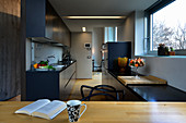 Long, narrow, open-plan kitchen with dark blue cupboards and pale wooden elements