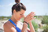 Reife Frau macht Yoga-Übung (Namasta-Geste) am Strand