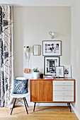 Retro sideboard and chair in corner with black-and-white photographs on wall