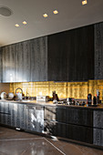 Black wooden cabinets and golden splashback in kitchen