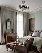 Leather armchair in elegant bedroom with high ceiling and antique bureau