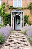 Gravel path lined by lavender beds leading to front door of country house with porch