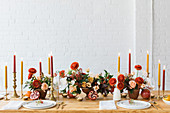 Festlich gedeckter Tisch mit roter Blumendeko, Früchten und Kerzen