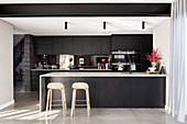 Zwei Barhocker an der Kücheninsel einer modernen schwarzen Küche