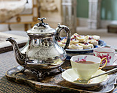 Silver teapot, teacups and pastries on tray