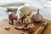 Onions, garlic and folding knife on wooden board