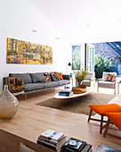 Hohes Wohnzimmer mit grauem Polstersofa, Coffeetable und Terrassenzugang