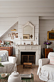 Slip covered armchairs with Gustavian style fireplace in tongue and groove living room of 18th century conversion