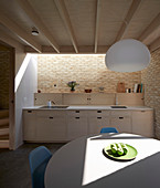 Round table in open-plan modern kitchen with counter, brick wall and skylight