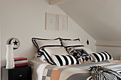 Black-and-white scatter cushions on double bed below sloping ceiling