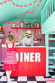 Children at counter in play house made to look like fifties diner